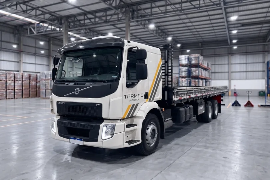Caminhão Volvo VM da Tarmac Logística, com carroceria aberta, dentro de um centro de distribuição