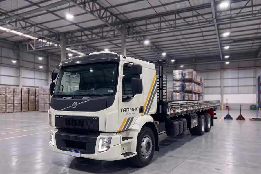 Caminhão Volvo VM da Tarmac Logística, com carroceria aberta, dentro de um centro de distribuição